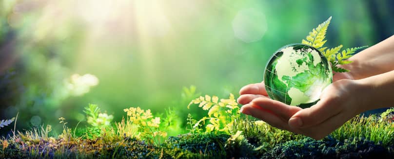 Hand-holds-green-glass-ball-with-world-map-in-front-of-a-green-fertile-soil-and-sky