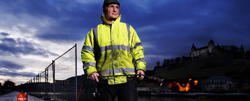Unkrautbekämpfung mit Flüssiggas in Flaschen - TEGA Bauarbeiter-in-Arbeitsklamotten-mit-Fluessiggas-Flasche-in-der-Hand-bei-Nacht