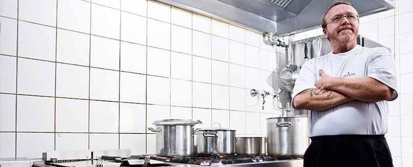 Kochen mit Flüssiggas in Flaschen - TEGA Mann-in-Kochbekleidung-steht-in-der-Kueche-mit-verschraenkten-Armen