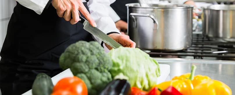 Koch-mit-Messer-in-der-Hand-zerkleinert-buntes-Gemuese-in-der-Kueche