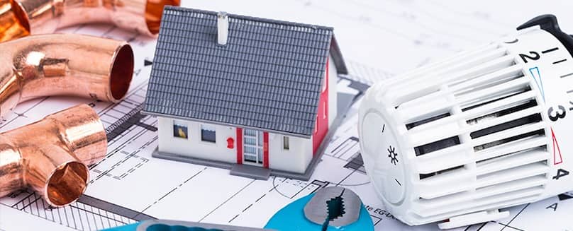 Heizen mit Flüssiggas - TEGA GmbH Miniatur-Haus-neben-Thermostat-und-kupferfarbenen-Rohren-auf-einer-Arbeitsfläche